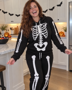 Woman laughing in a Halloween-decorated kitchen wearing the Skele-Oodie skeleton hoodie and jogger set